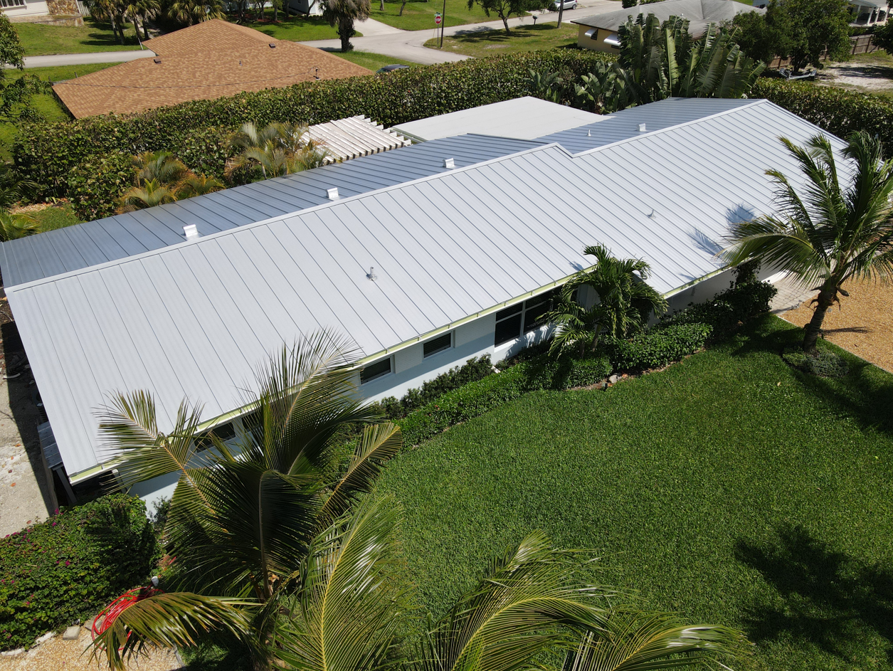 An aerial view of a house with a white roof surrounded by palm trees.
