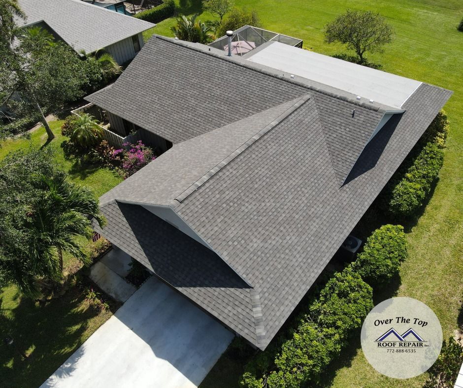 Aerial view of a gray-shingled house with a multi-gabled roof and green lawn