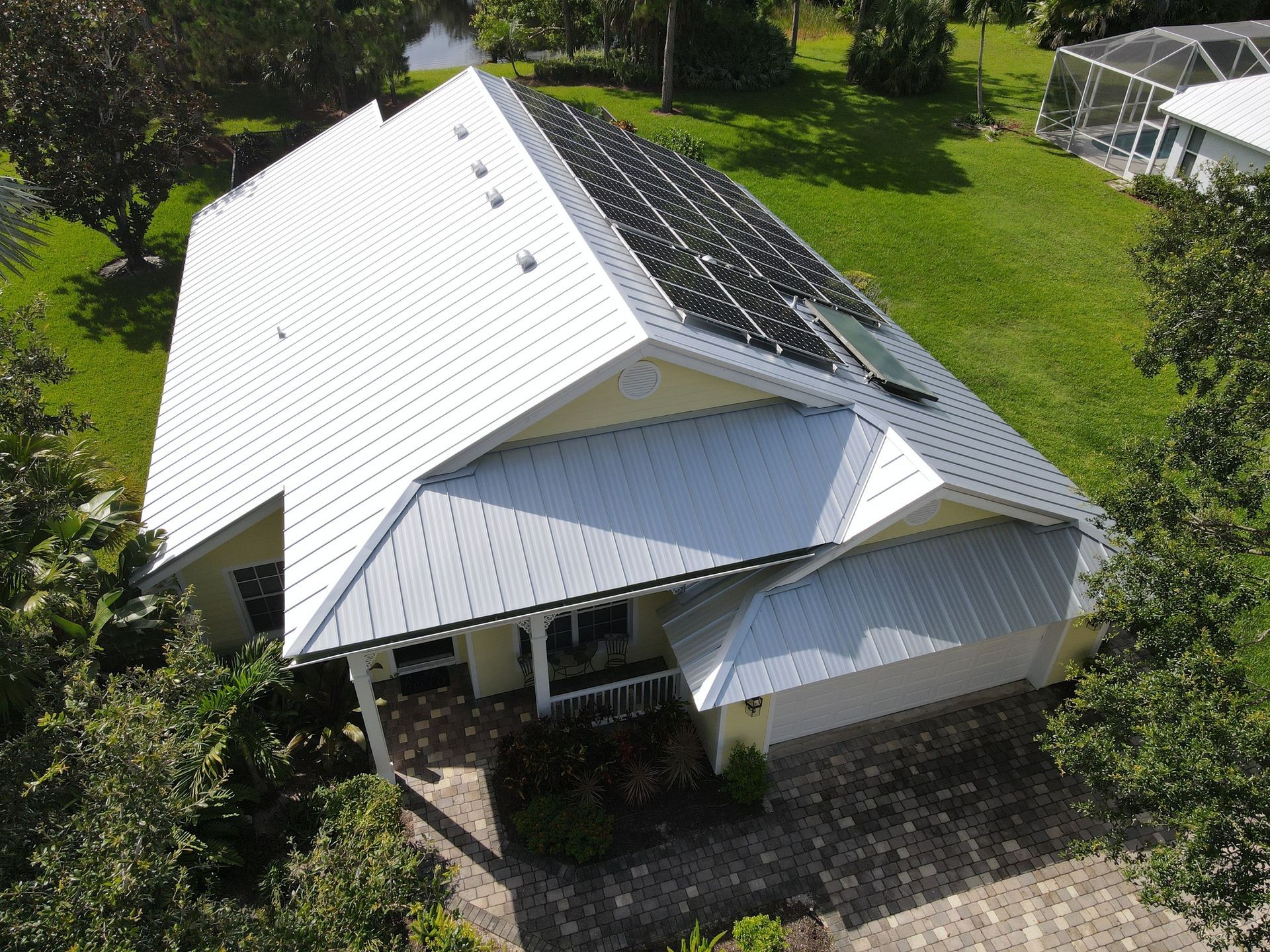 Aerial view of a white house with a dark solar-panel roof surrounded by green lawn.