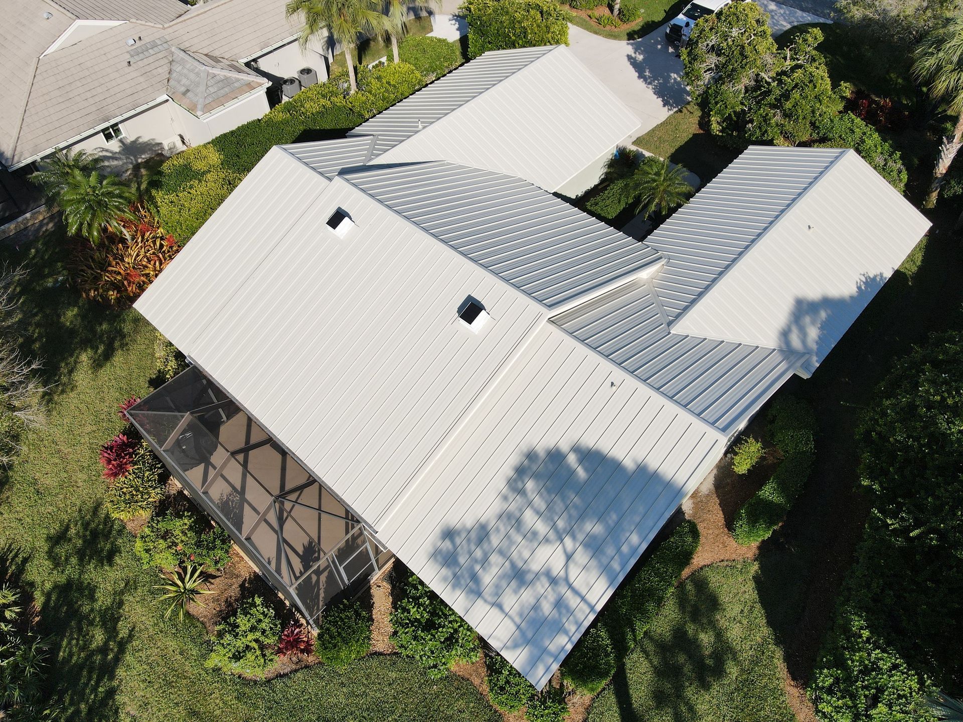 Aerial view of a white-roofed house surrounded by lush green trees and vegetation.