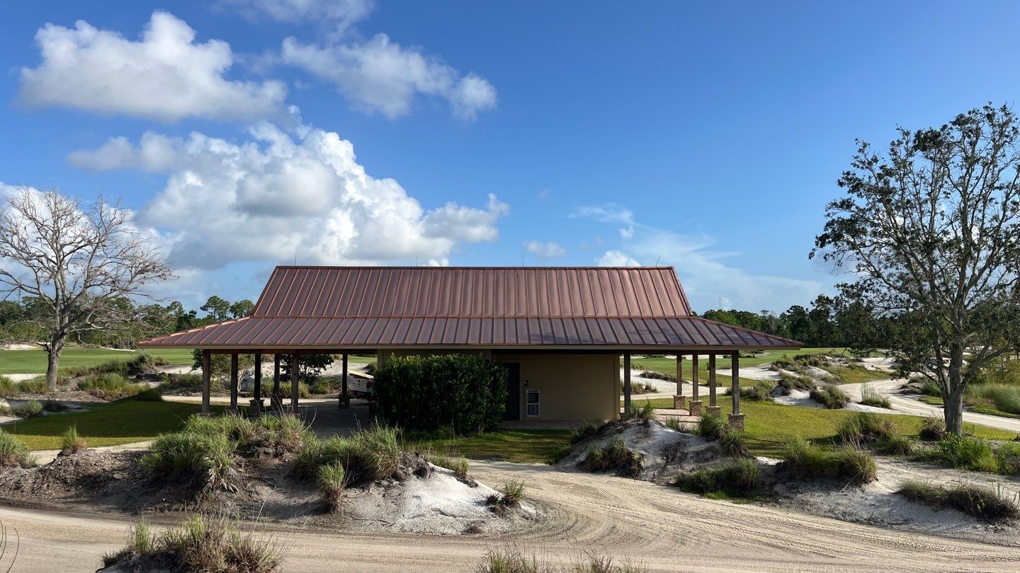 Small pavilion with a red roof in a sunny landscaped park under a blue sky with clouds