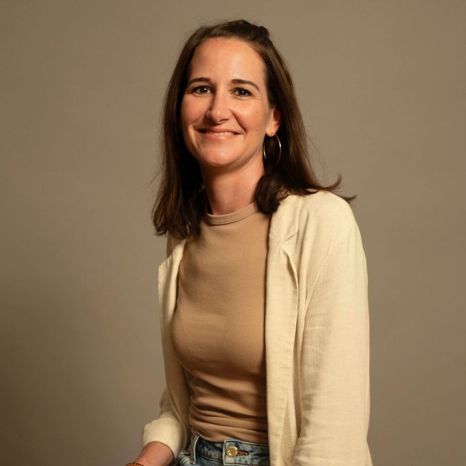 Lächelnde Frau in cremefarbener Strickjacke und hellbraunem Top vor schlichtem beigefarbenem Hintergrund