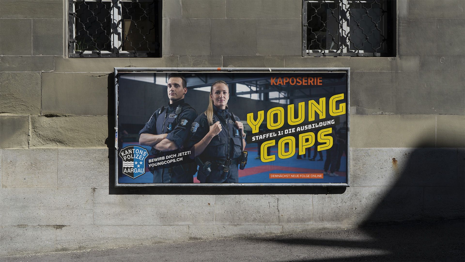 Plakat für „Young Cops“ auf einer Steinmauer, mit zwei Polizisten und fettgedrucktem gelbem Titeltext.