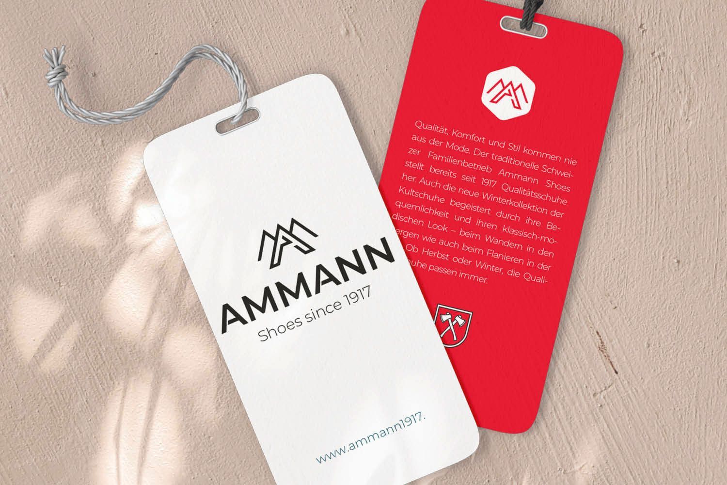 Zwei hängende AMMANN-Kleidungsetiketten, eines weiß und eines rot, auf beigefarbenem, strukturiertem Hintergrund
