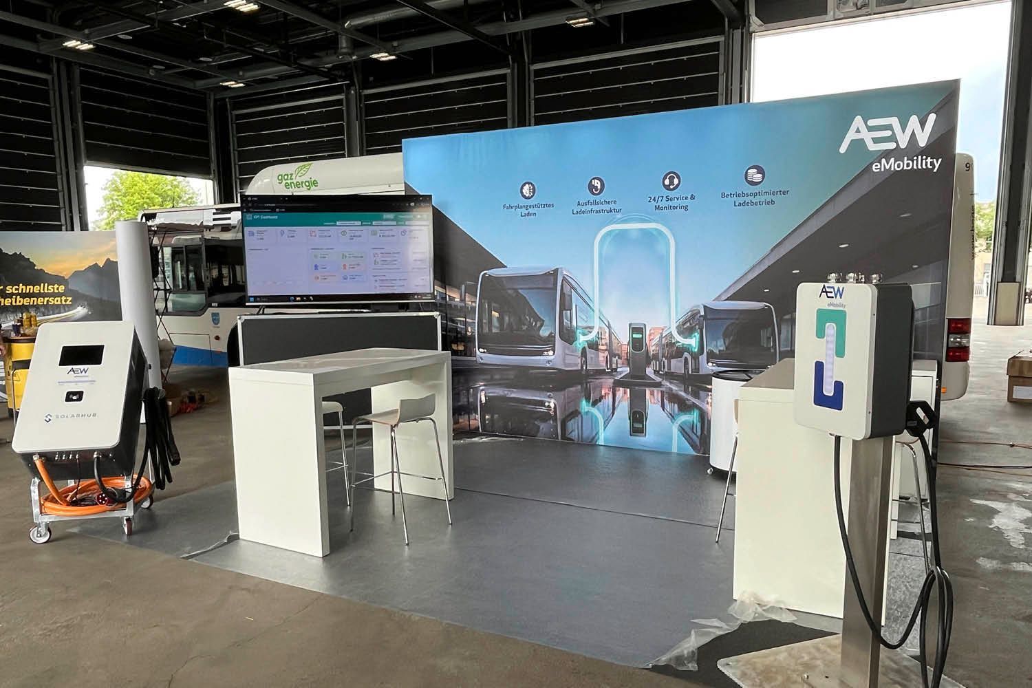 Messestand mit großer Rückwand, Präsentationstischen und Ausrüstung auf einer Indoor-Messe.