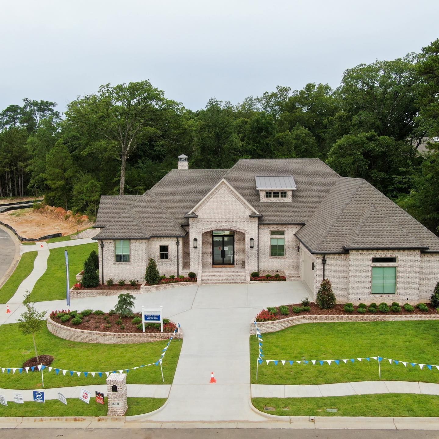 Exterior view of a light brick house with a gray roof and driveway, lush green lawn, and landscaping.