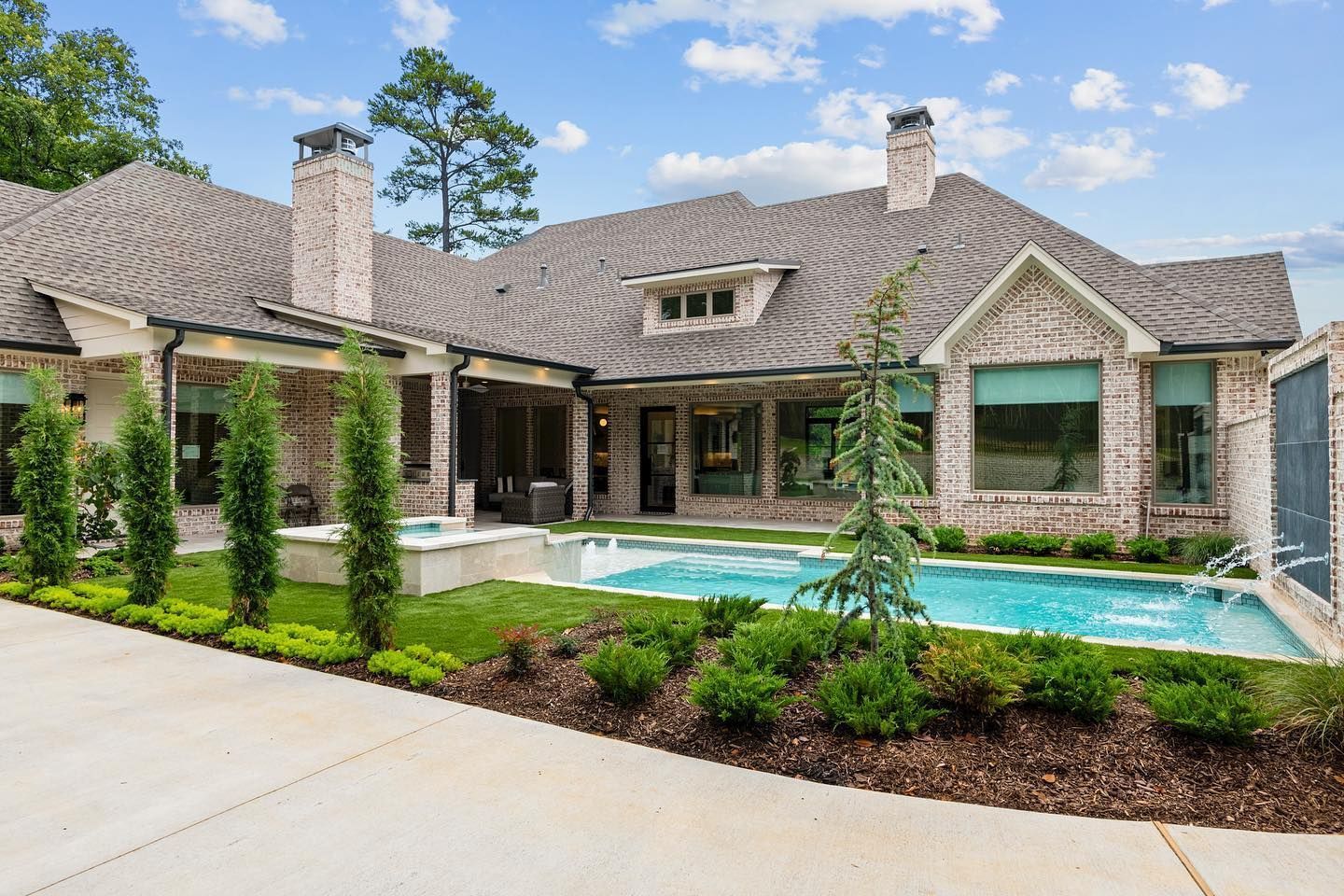 Luxurious brick home with a pool, lush landscaping, and a clear blue sky.