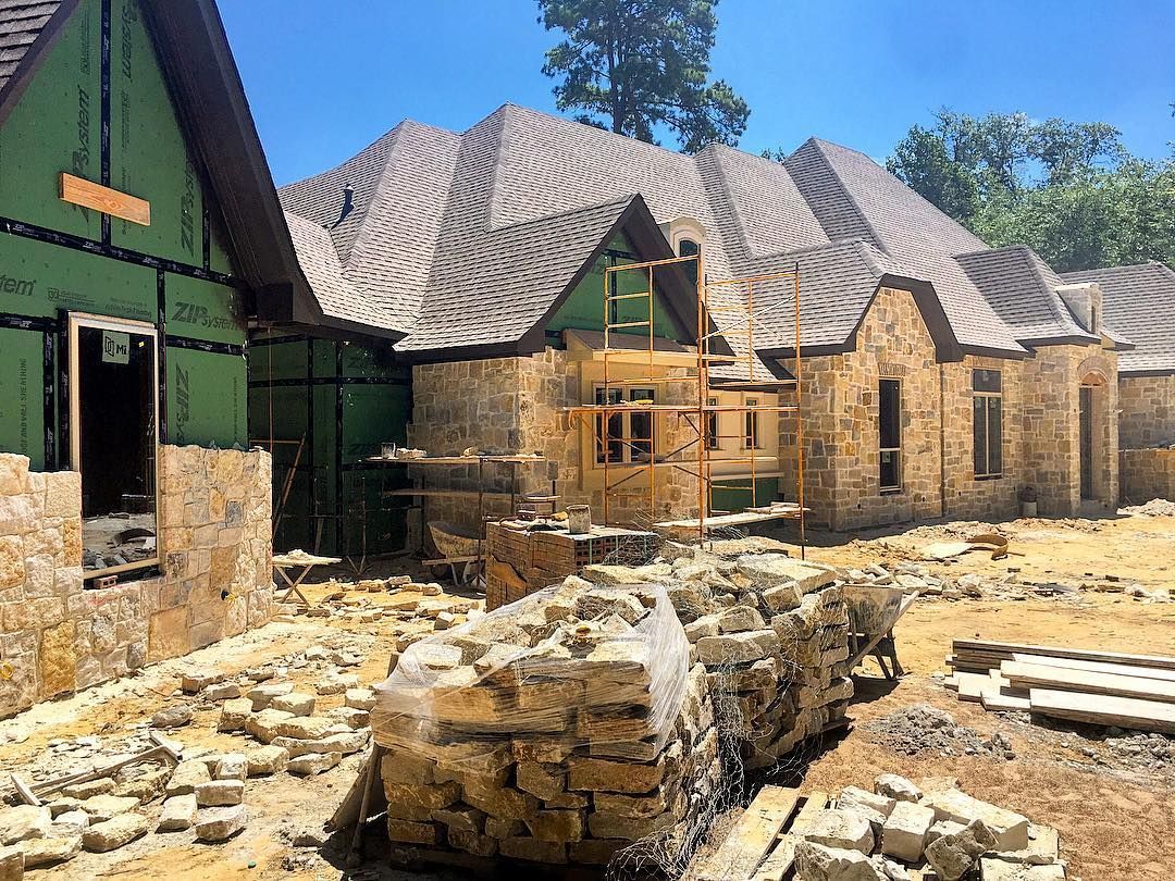 A house under construction with stone facade and a complex, patterned roof.