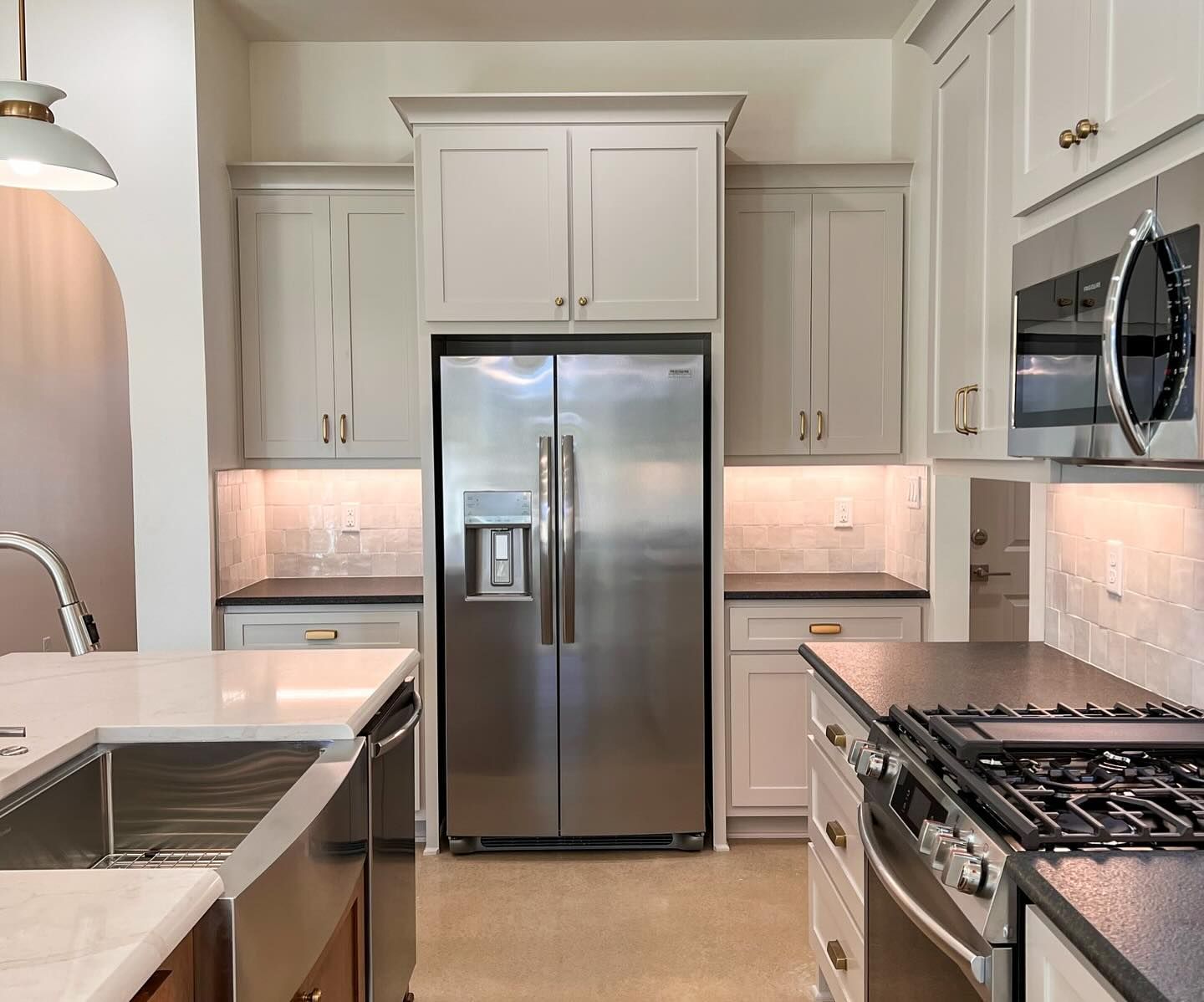 Modern kitchen with stainless steel refrigerator, gray cabinets, and black countertops.
