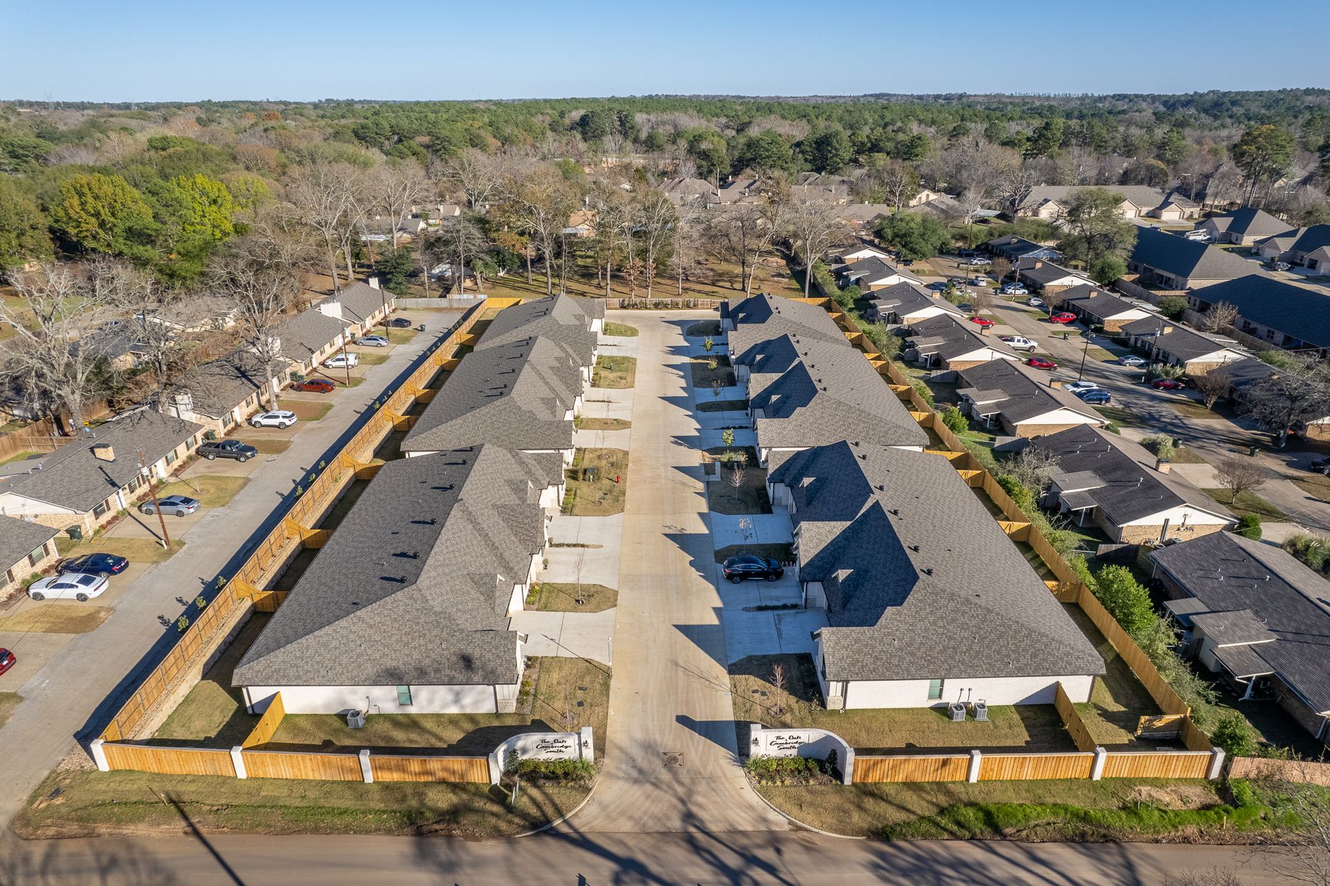 Aerial view of a row of townhouses with gray roofs and a shared driveway, surrounded by a residential area.