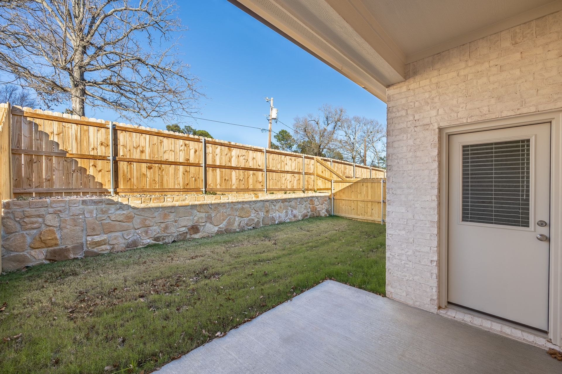 Concrete patio overlooking backyard with grass, wooden fence, and white door.