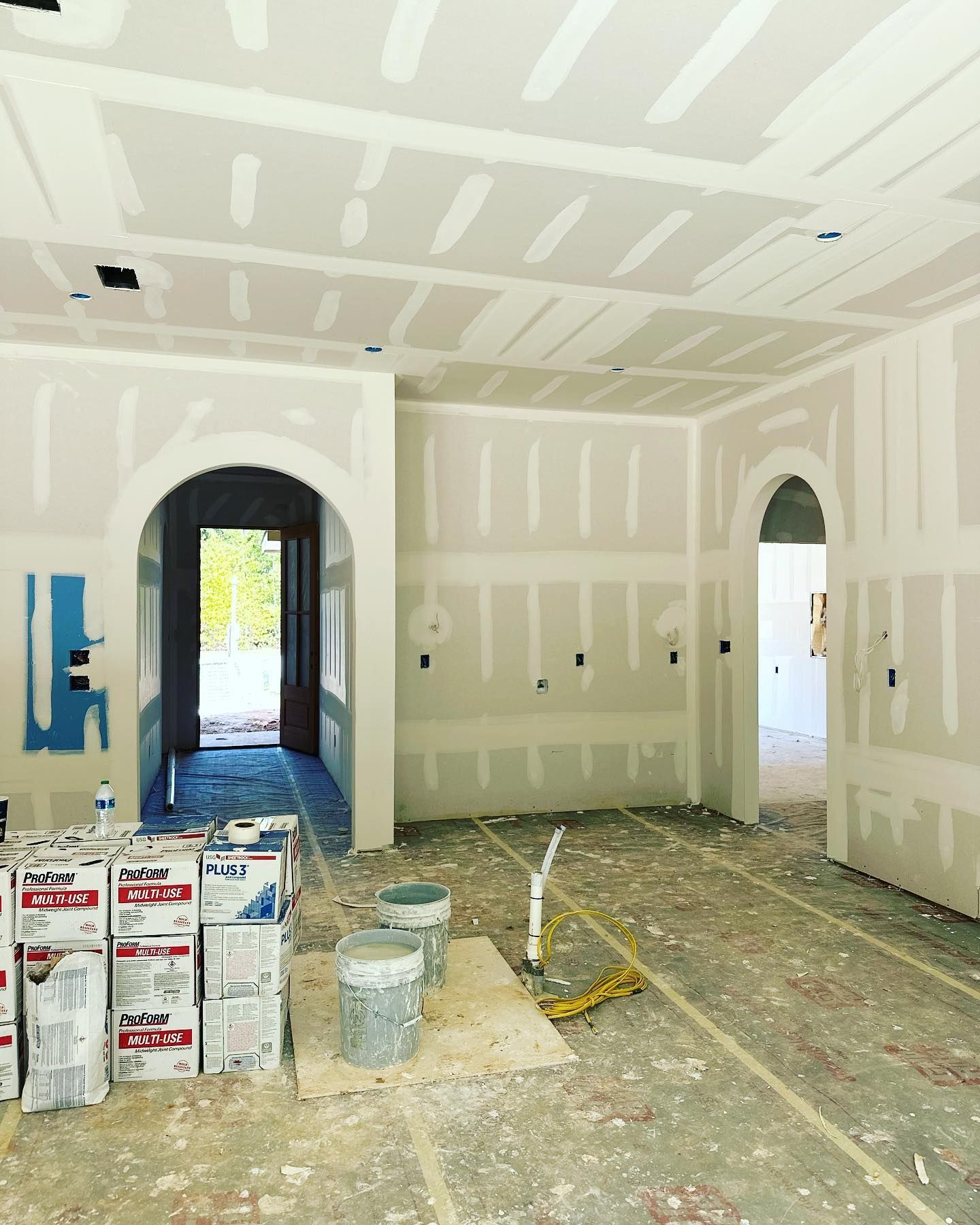 Interior construction site with drywall installed; arched doorways, bare floors, supplies.