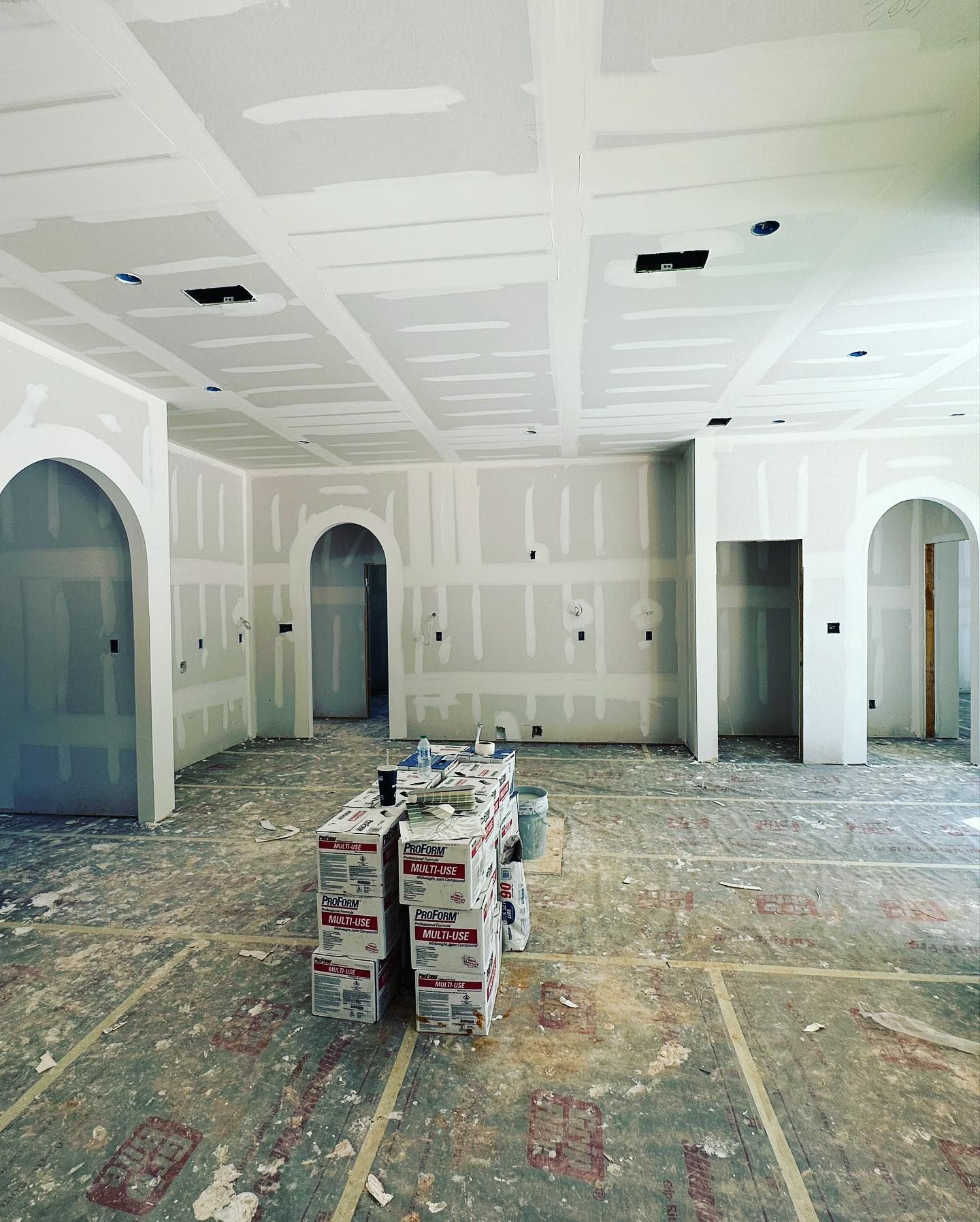 Interior of a room under construction, with drywall on walls and ceiling, arched doorways, and debris on the floor.