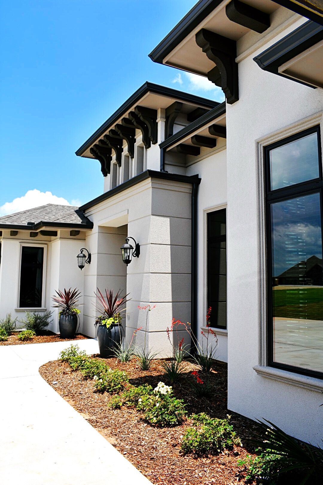 White stucco house with dark trim and large windows, surrounded by landscaping.