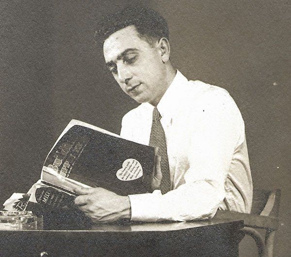 A man in a white shirt and tie is reading a book