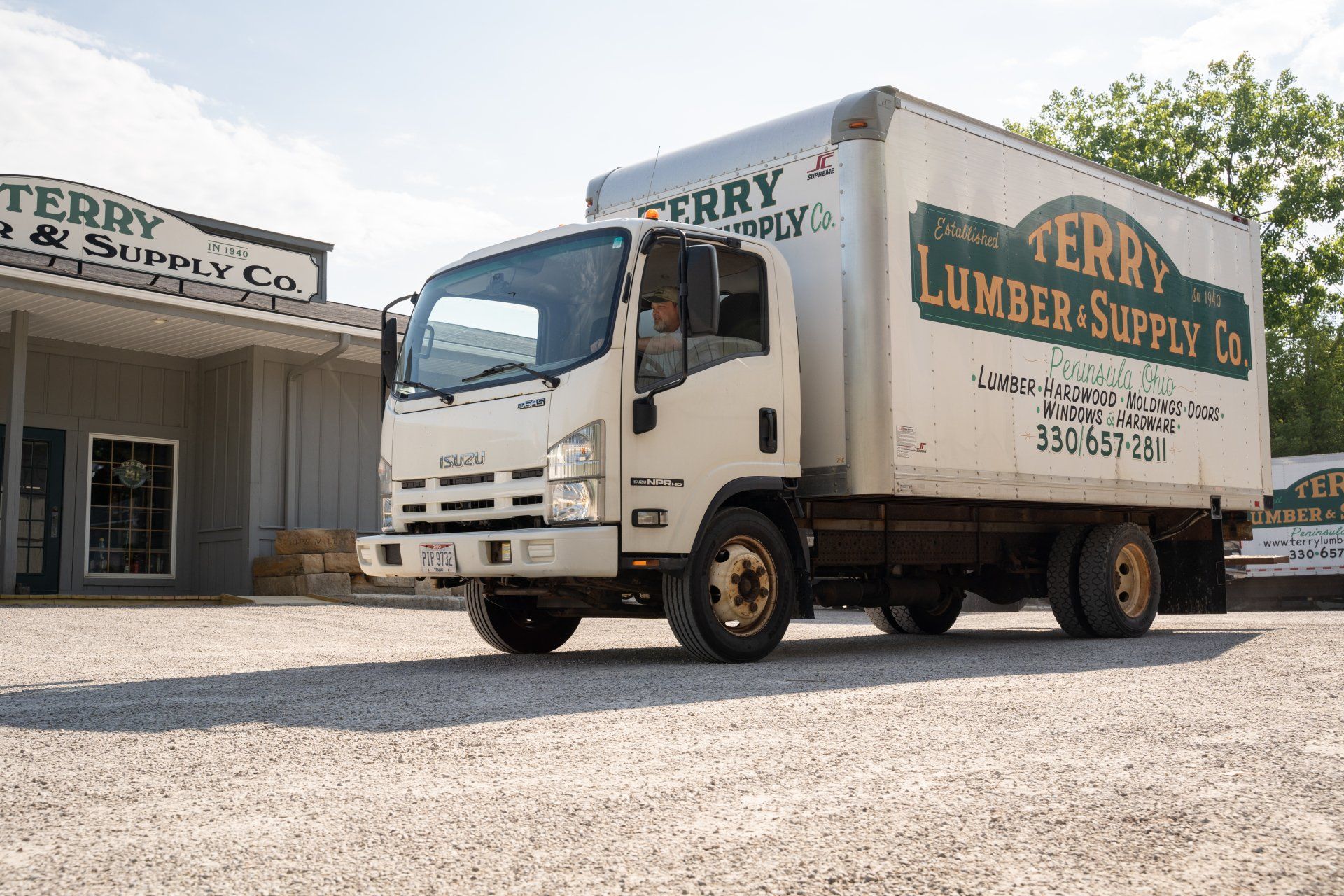 A white lumber supply truck is parked in front of a building.