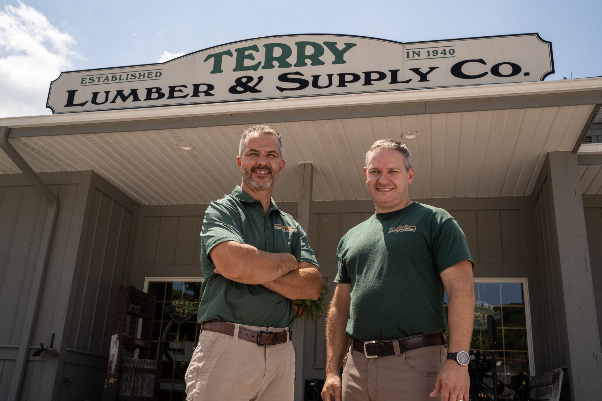 Two men are standing in front of a sign for terry lumber & supply co.