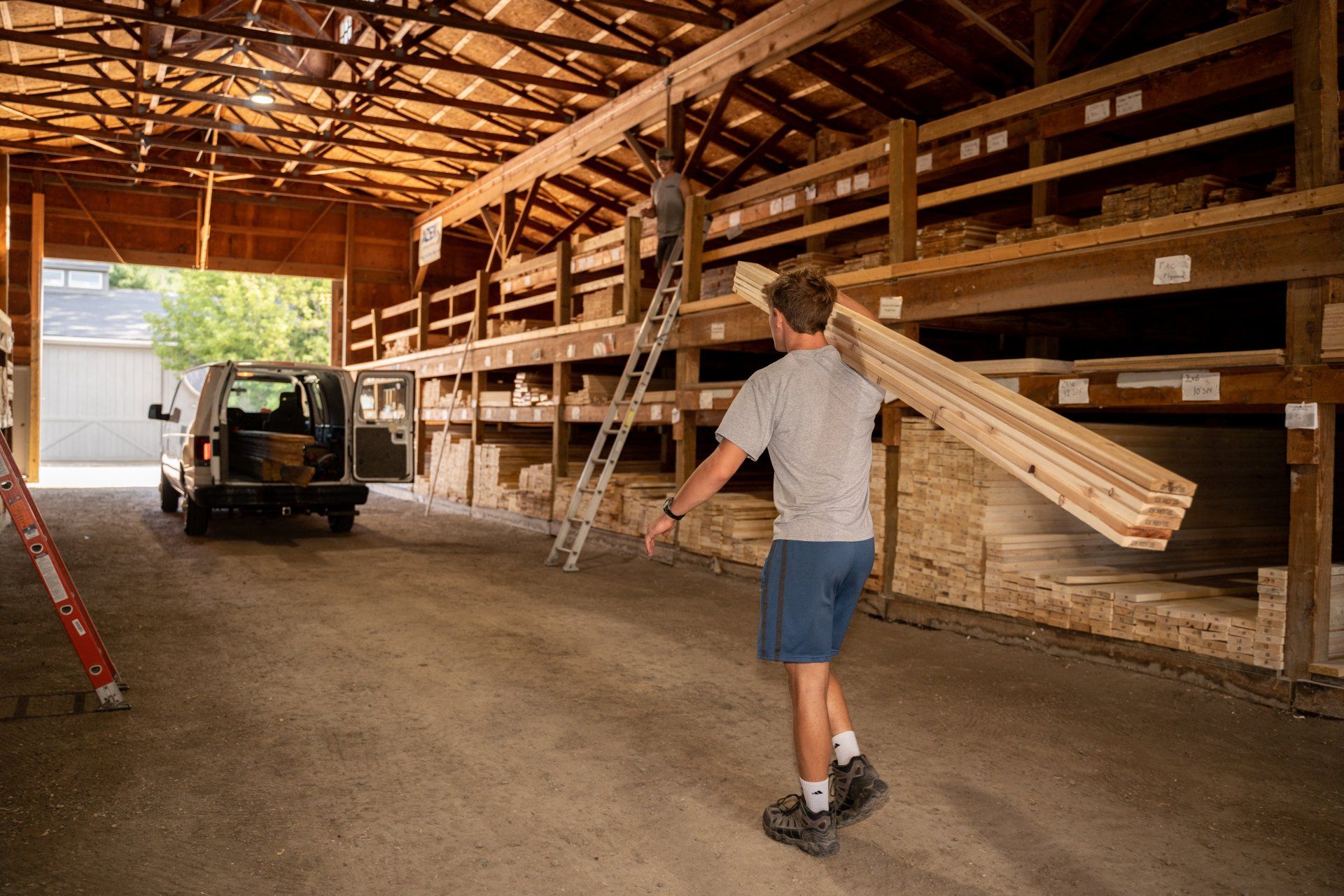 A man is carrying a large piece of wood in a warehouse.