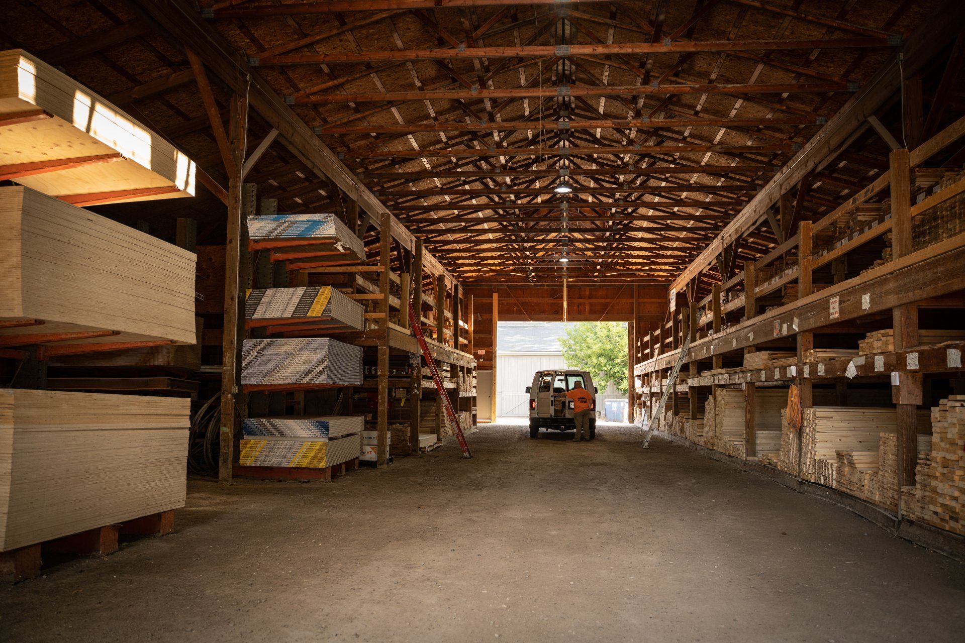 A truck is parked inside of a large warehouse filled with wood.