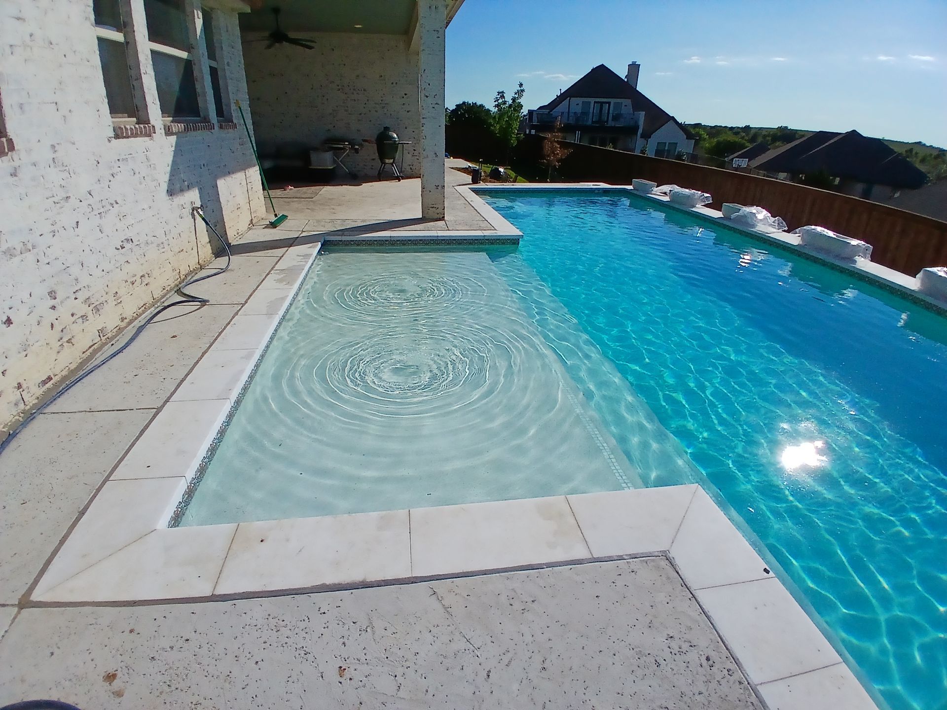Poolside patio with a small shallow pool, turquoise water, and a house in the background