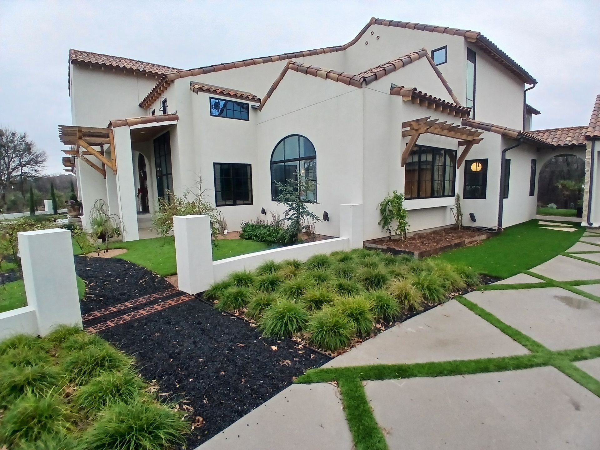 Modern white stucco home with dark roof, arched windows, and landscaped front yard with stone walkway