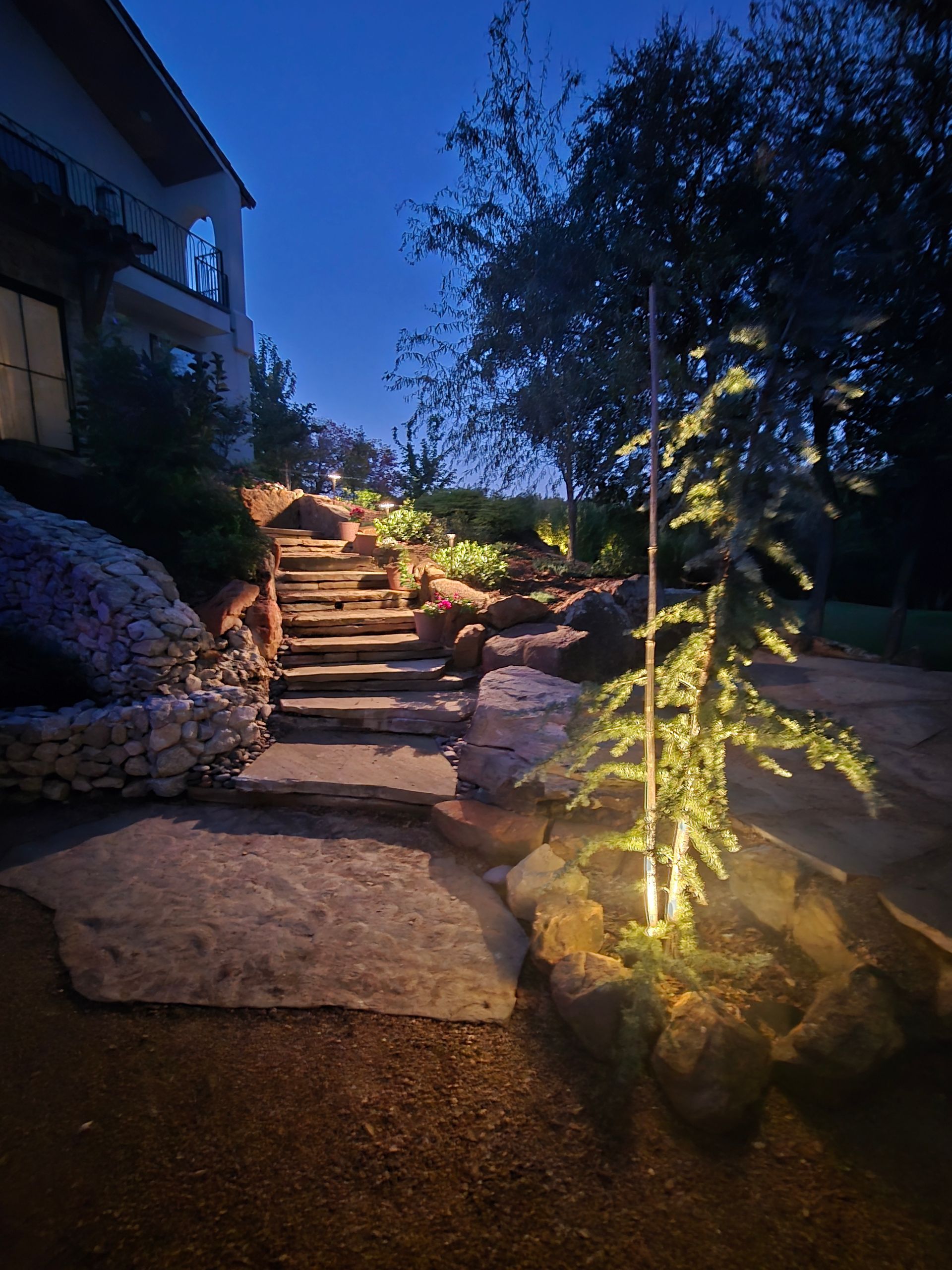 Illuminated stone steps in a garden at dusk, with trees and warm landscape lighting