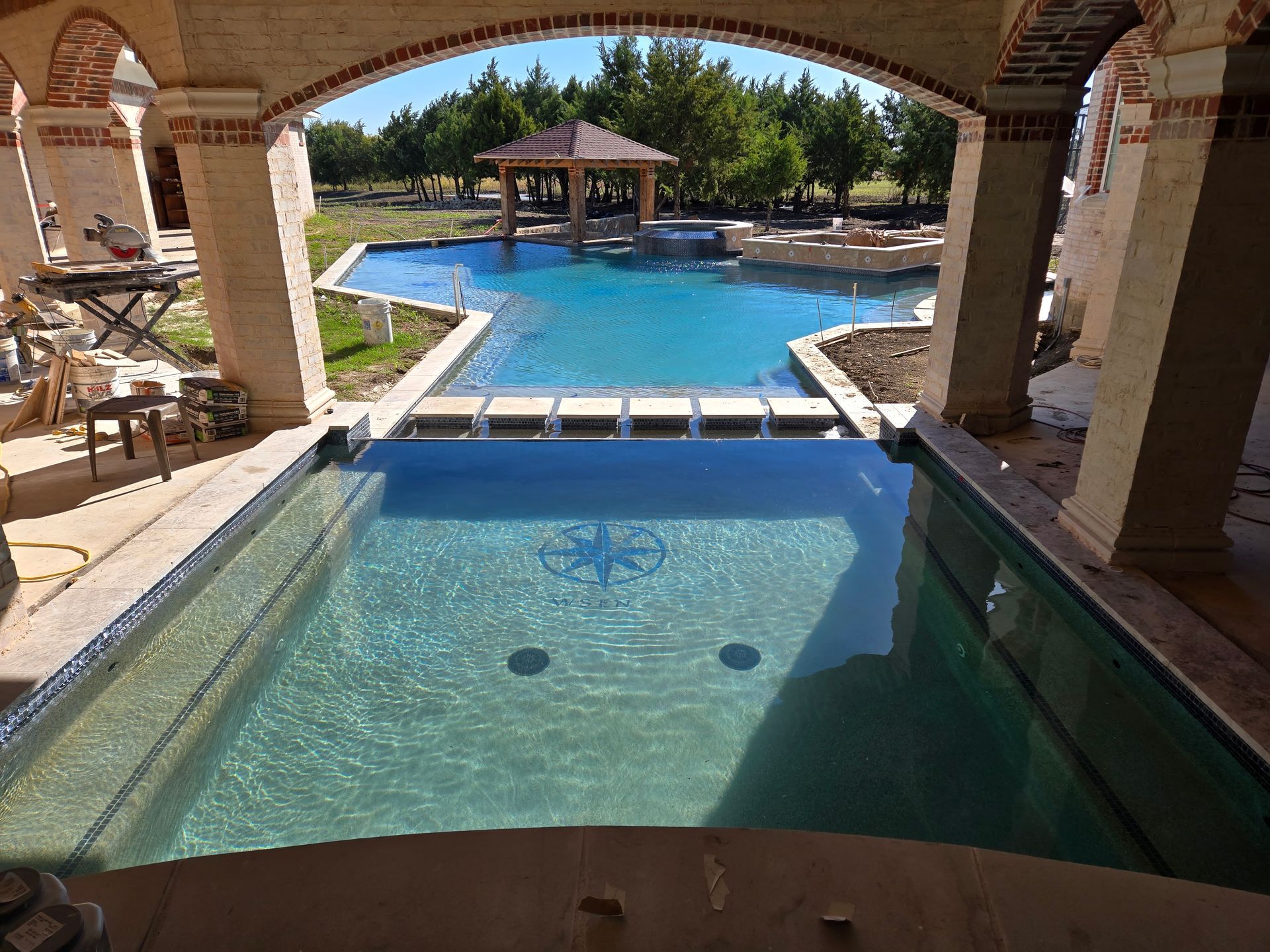 Covered resort pool with a shallow tanning ledge and arched stone columns overlooking a larger pool area