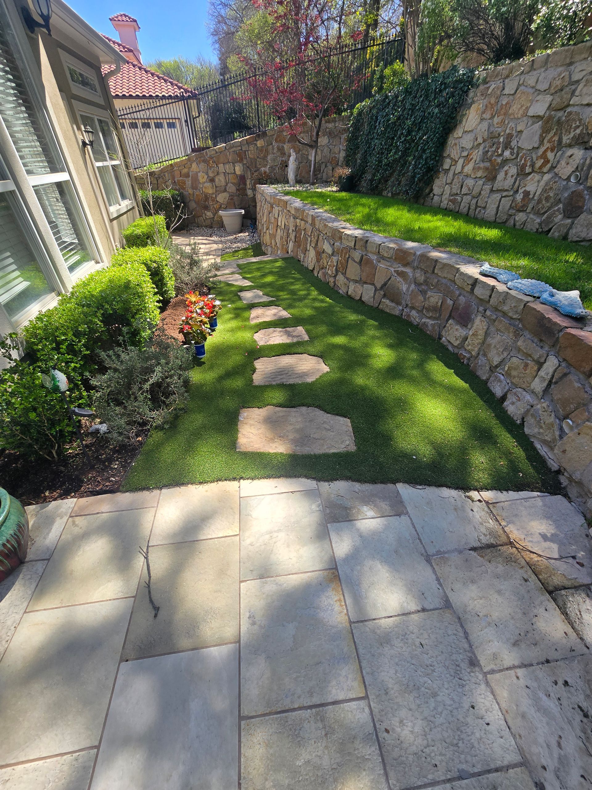 Stone stepping path through a narrow green garden beside a house and retaining wall