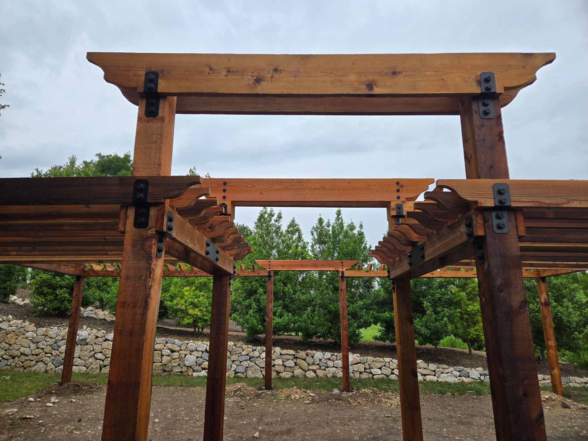 Wooden pergola structure in a landscaped garden with gravel paths and trees in the background