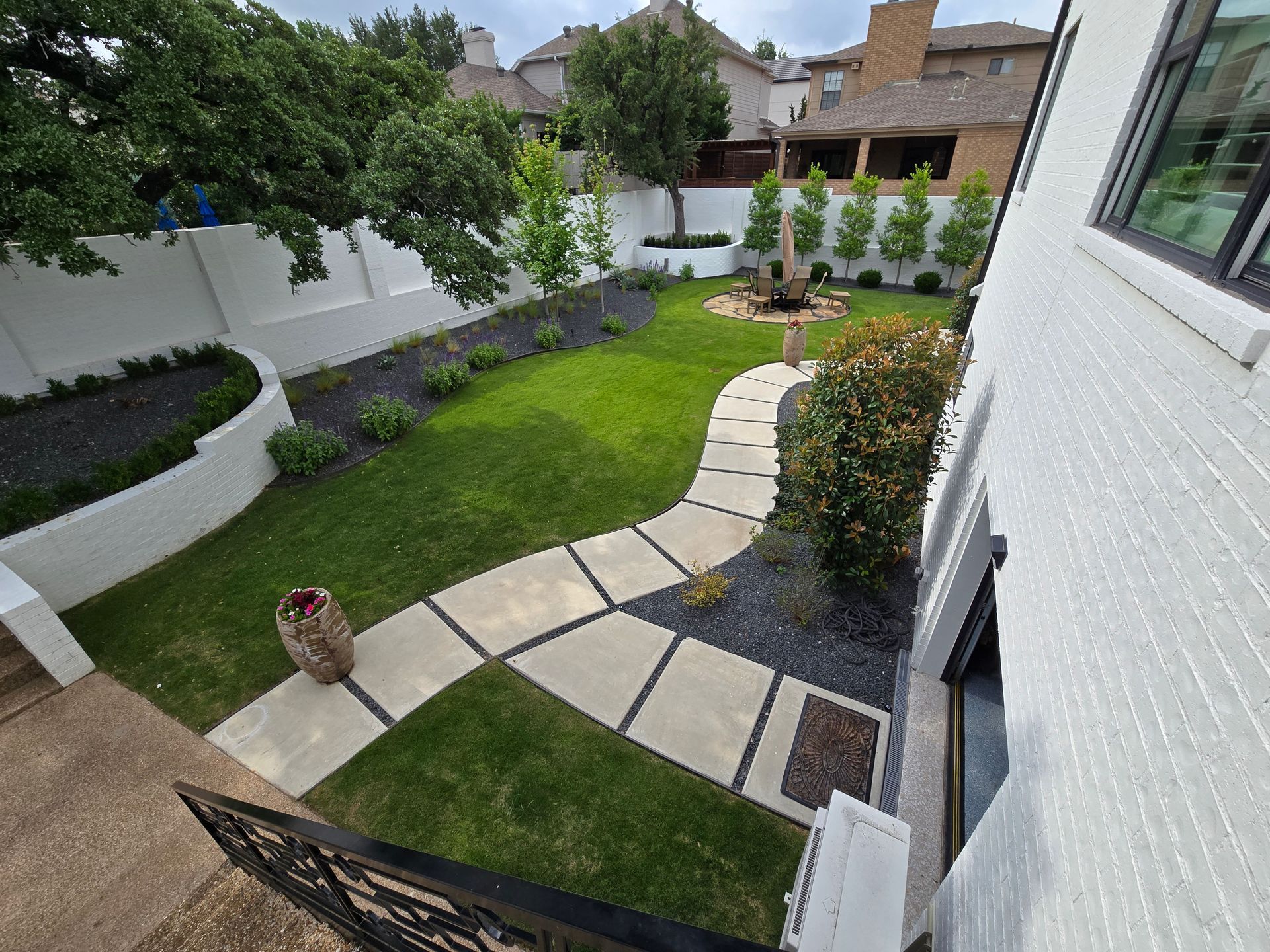 Curved stone path through a small green backyard garden beside a white house