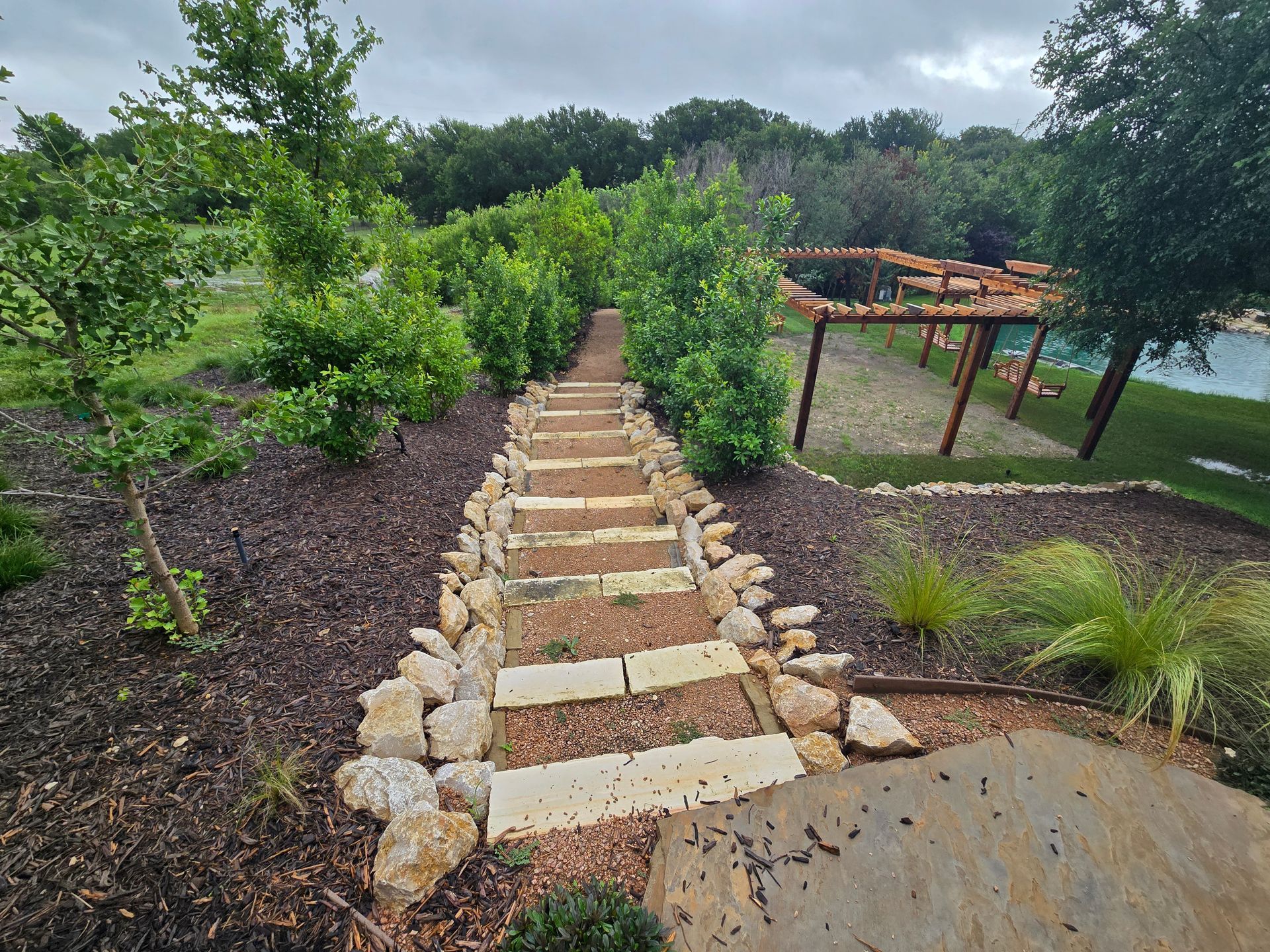 Stone steps through a landscaped garden lead uphill past greenery and a pond on the right.