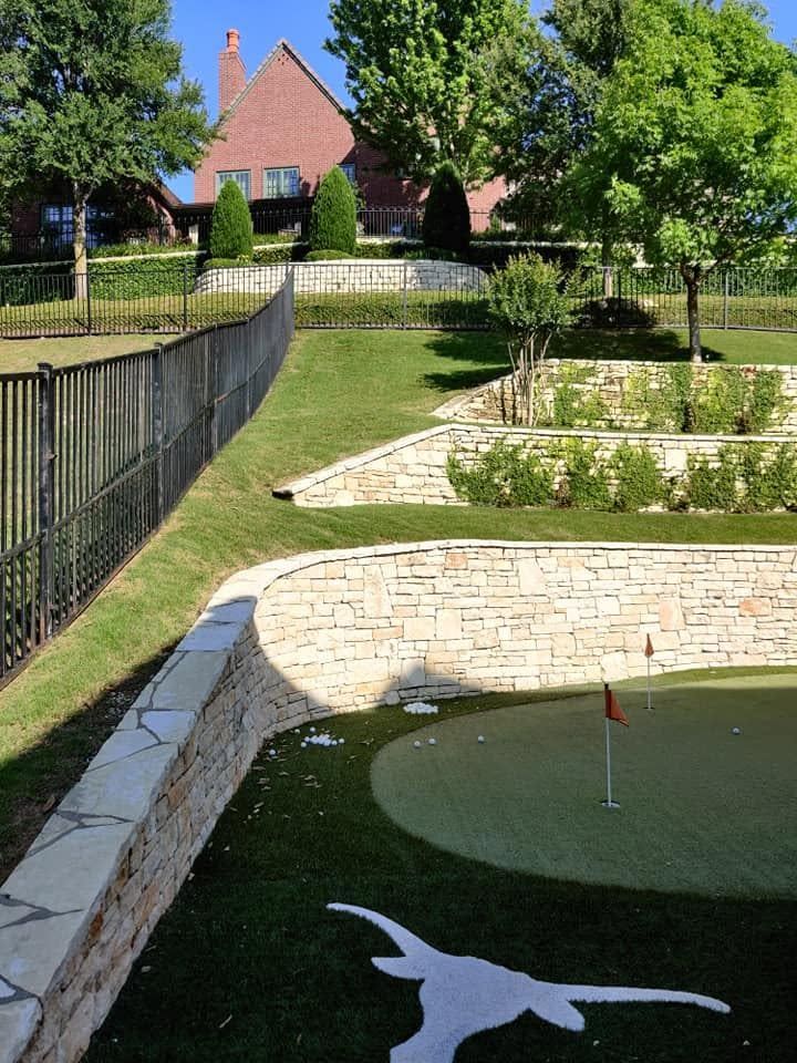 Landscaped garden with stone walls, black fence, and red-roofed houses in the background