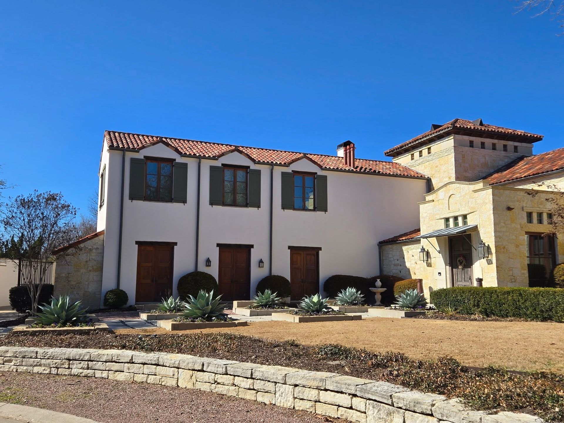 Spanish-style house with white stucco, red tile roof, and stone accents under a blue sky