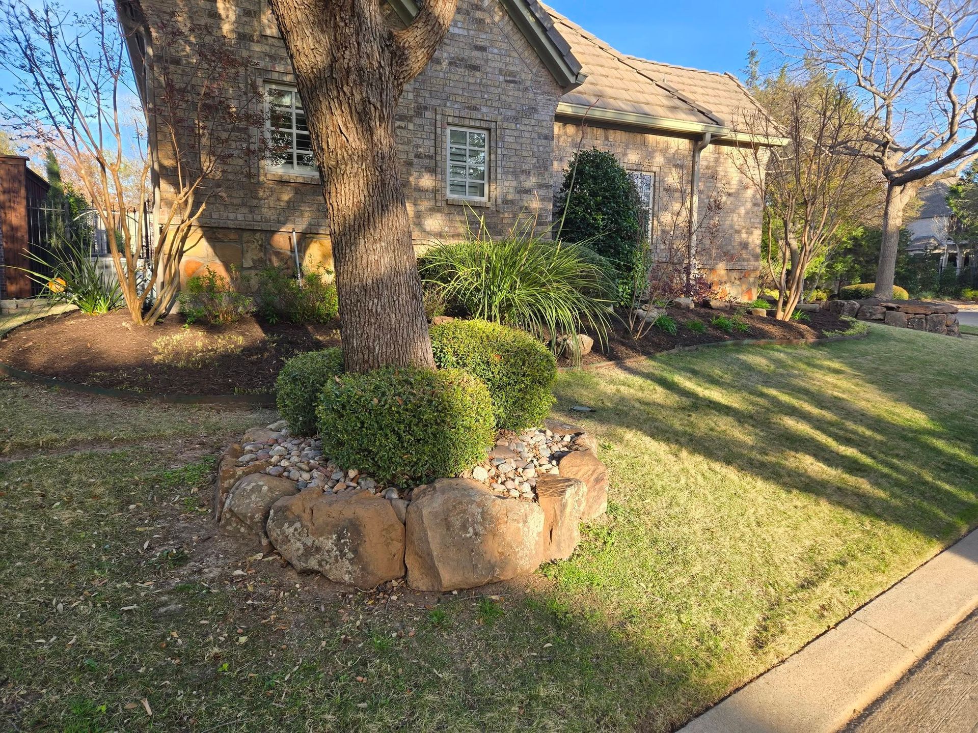 Stone house with a manicured front yard, shrubs, and a circular flower bed by the walkway.