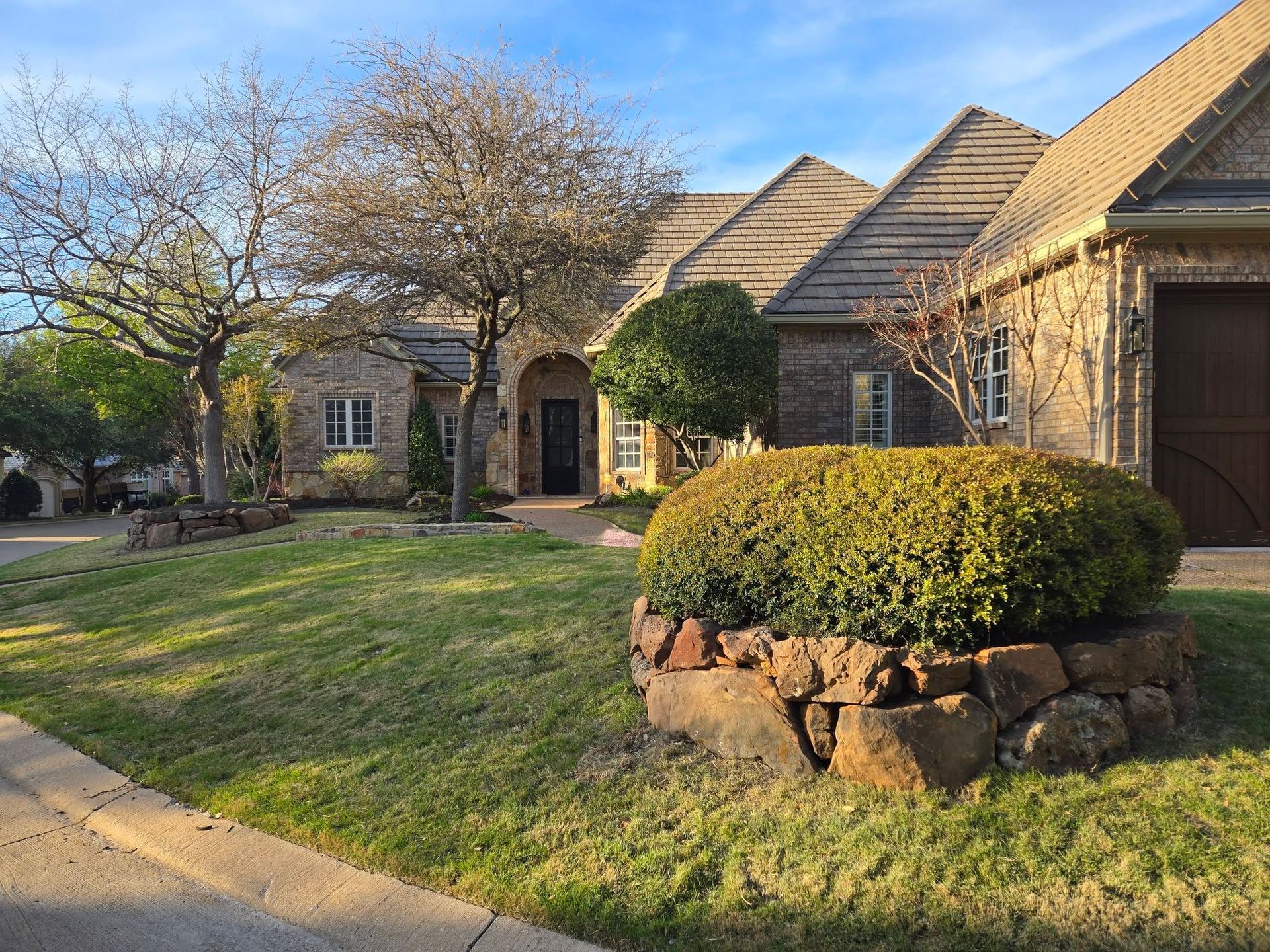 Suburban house with manicured lawn, leafless tree, and stone planter in front yard
