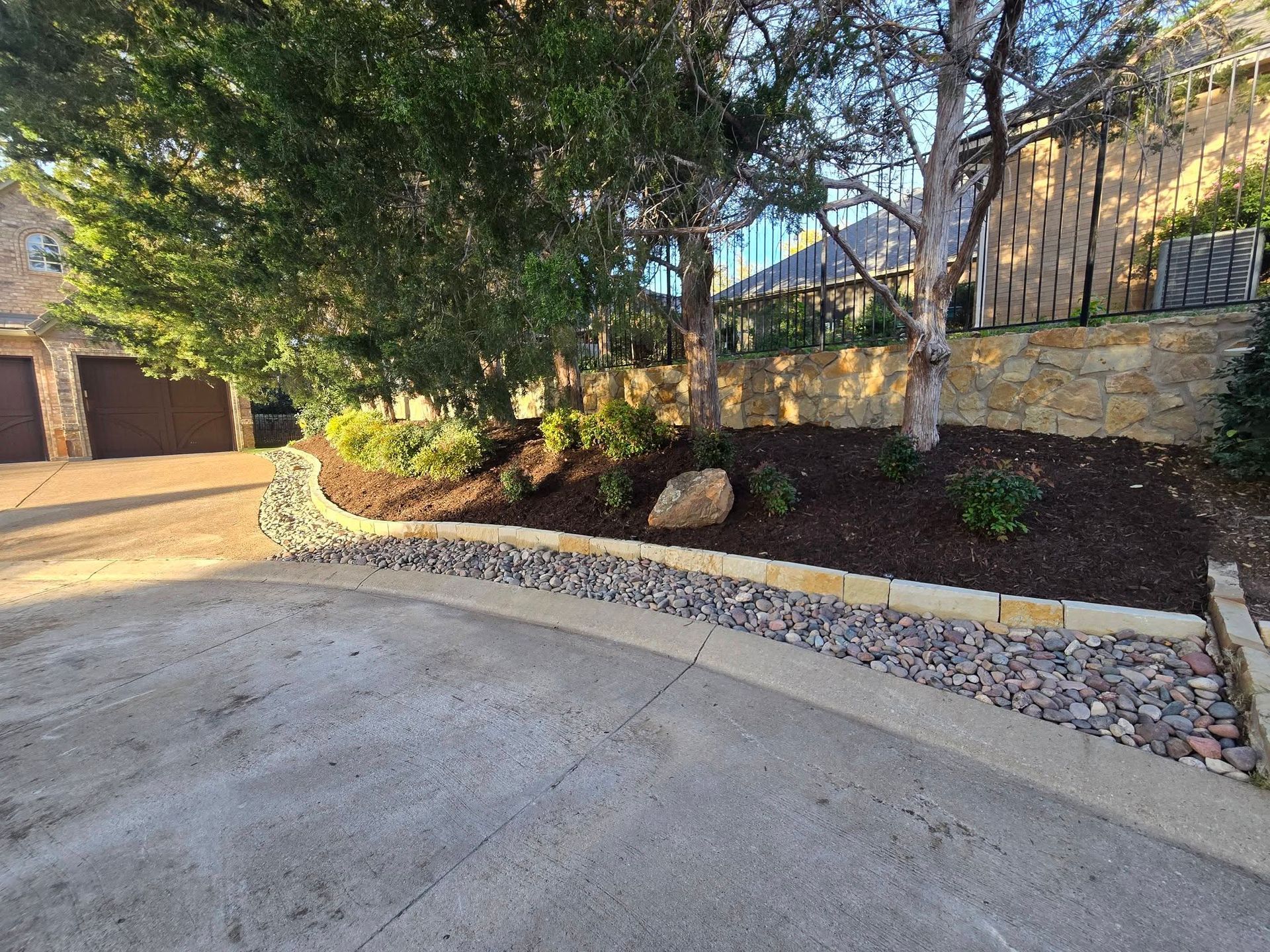 Driveway beside stone wall, trees, and landscaped garden in a residential area