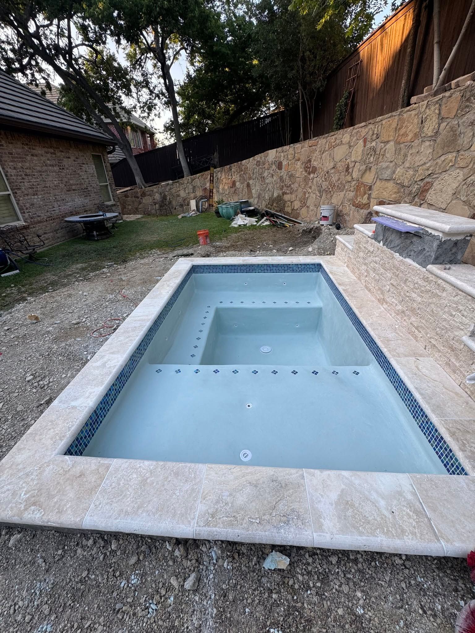 Empty rectangular in-ground pool in a stone-lined backyard with steps and surrounding gravel patio