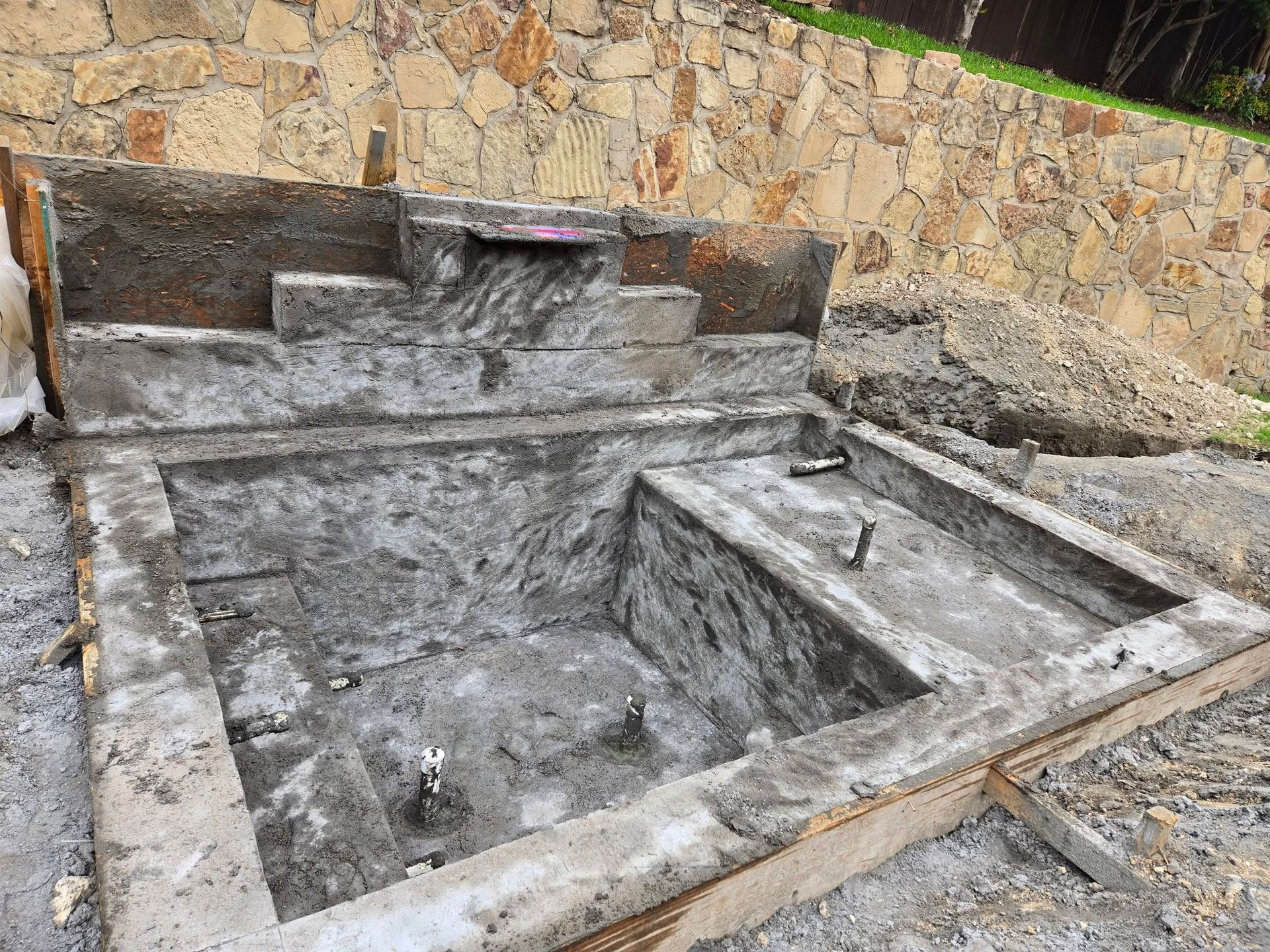 Concrete fountain basin and stone wall with a small water channel in an outdoor courtyard
