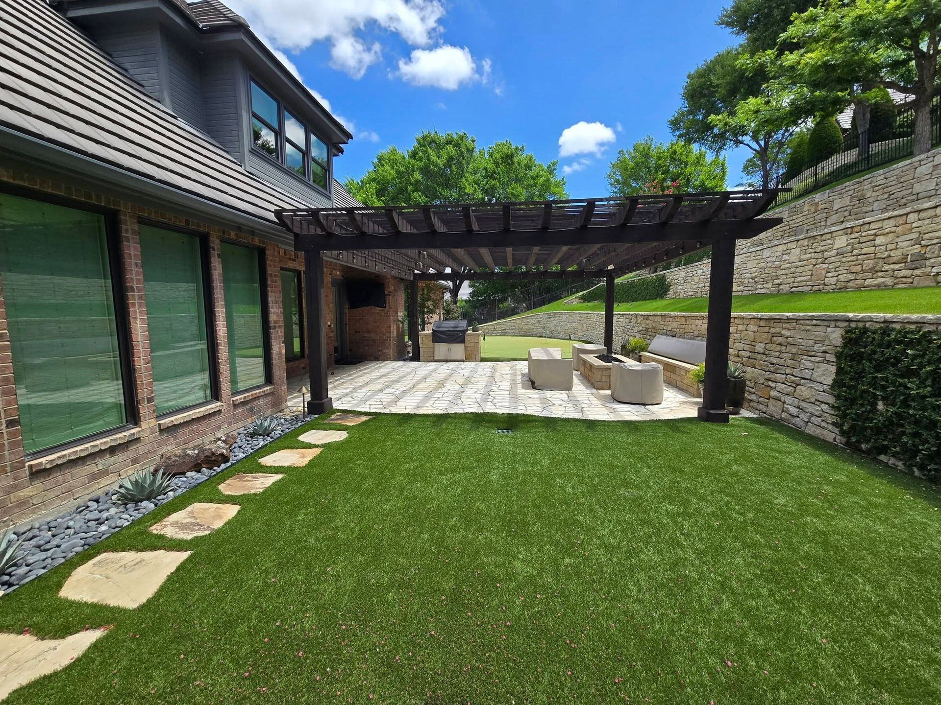Backyard patio with pergola, stone walkway, green lawn, and modern house exterior