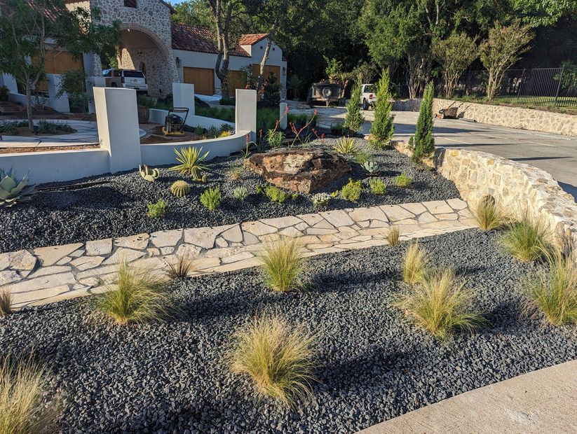 Modern landscaped garden with stone paths, gravel beds, shrubs, and a low stone wall near a house
