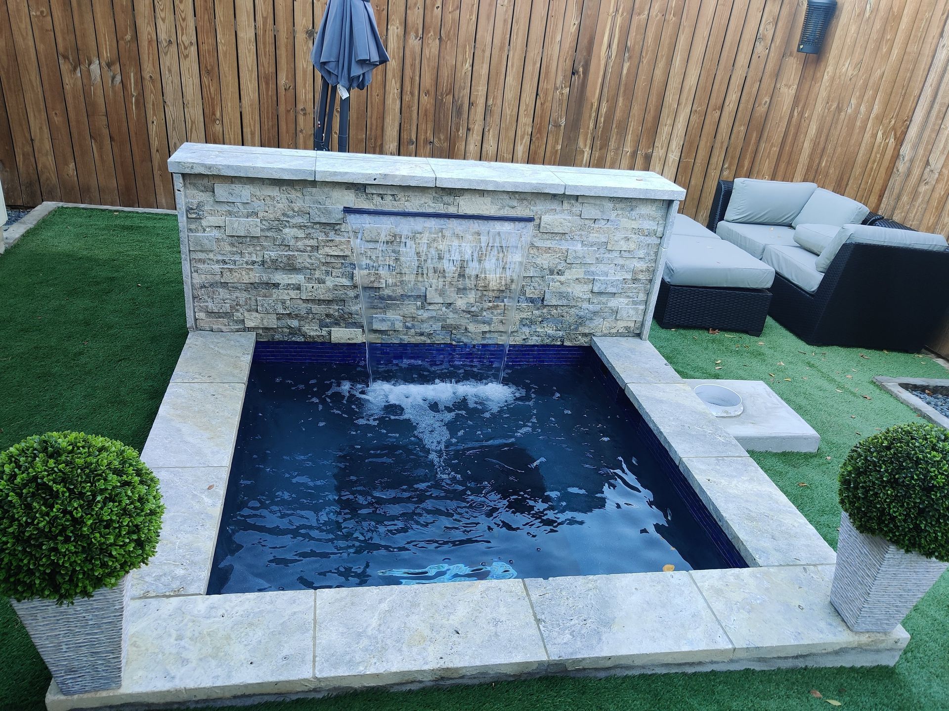 Small backyard stone plunge pool with a built-in waterfall wall and lounge chairs beside it