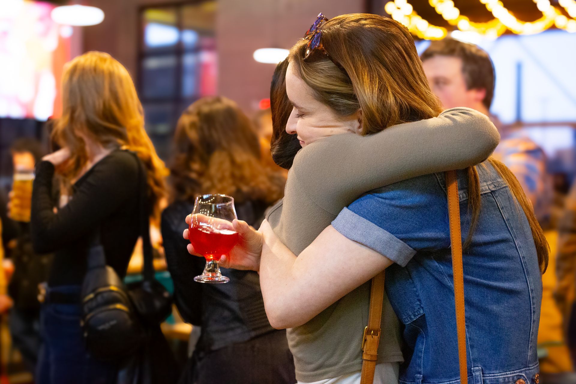 A woman is hugging another woman while holding a glass of wine.