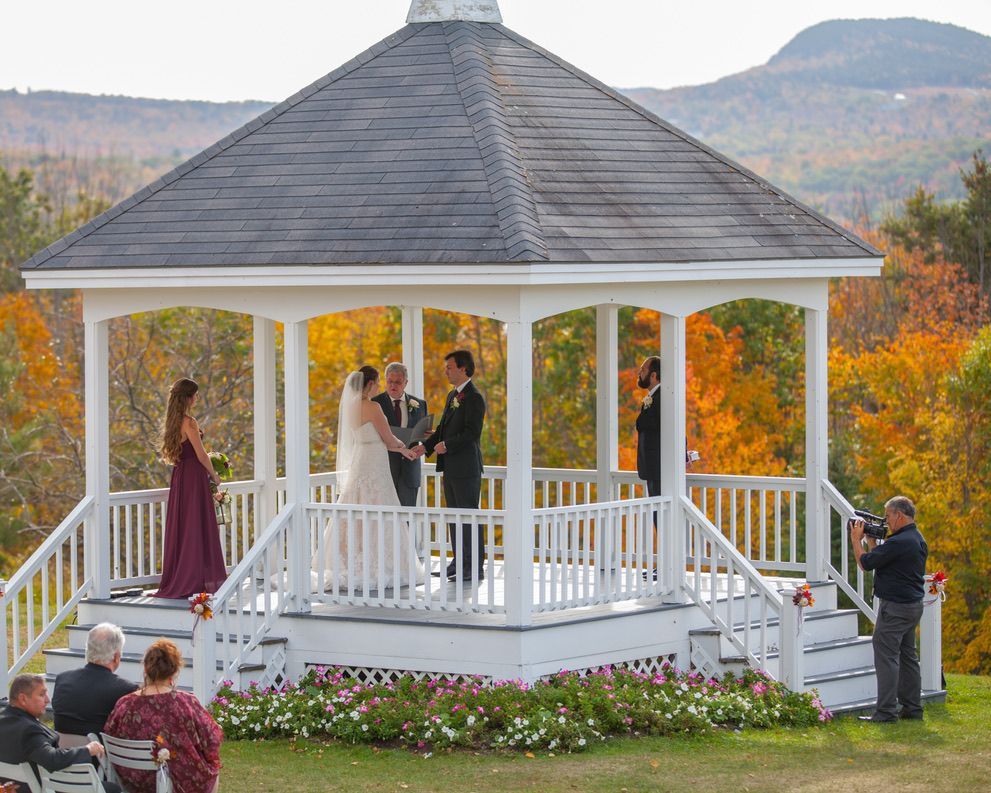 A man is taking a picture of a bride and groom in a gazebo.