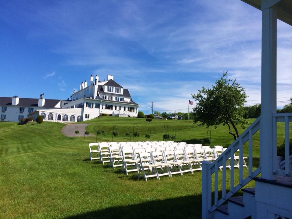 A row of white chairs are lined up in a grassy field in front of a large white building.