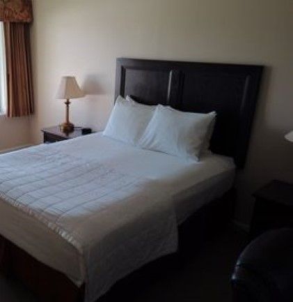 A hotel room with a bed , nightstand , lamp and window.