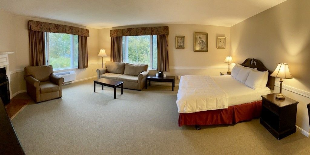A hotel room with a king size bed , couch , chair and fireplace.