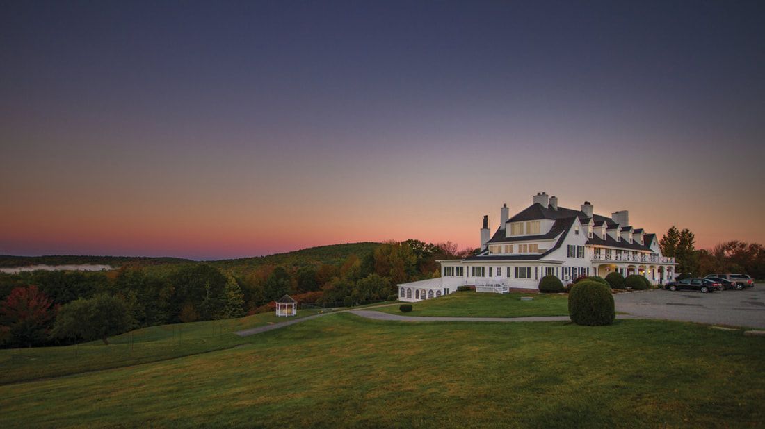 A large white house is sitting on top of a grassy hill at sunset.