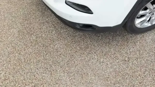 White car bumper, black grill, on a gravel surface.