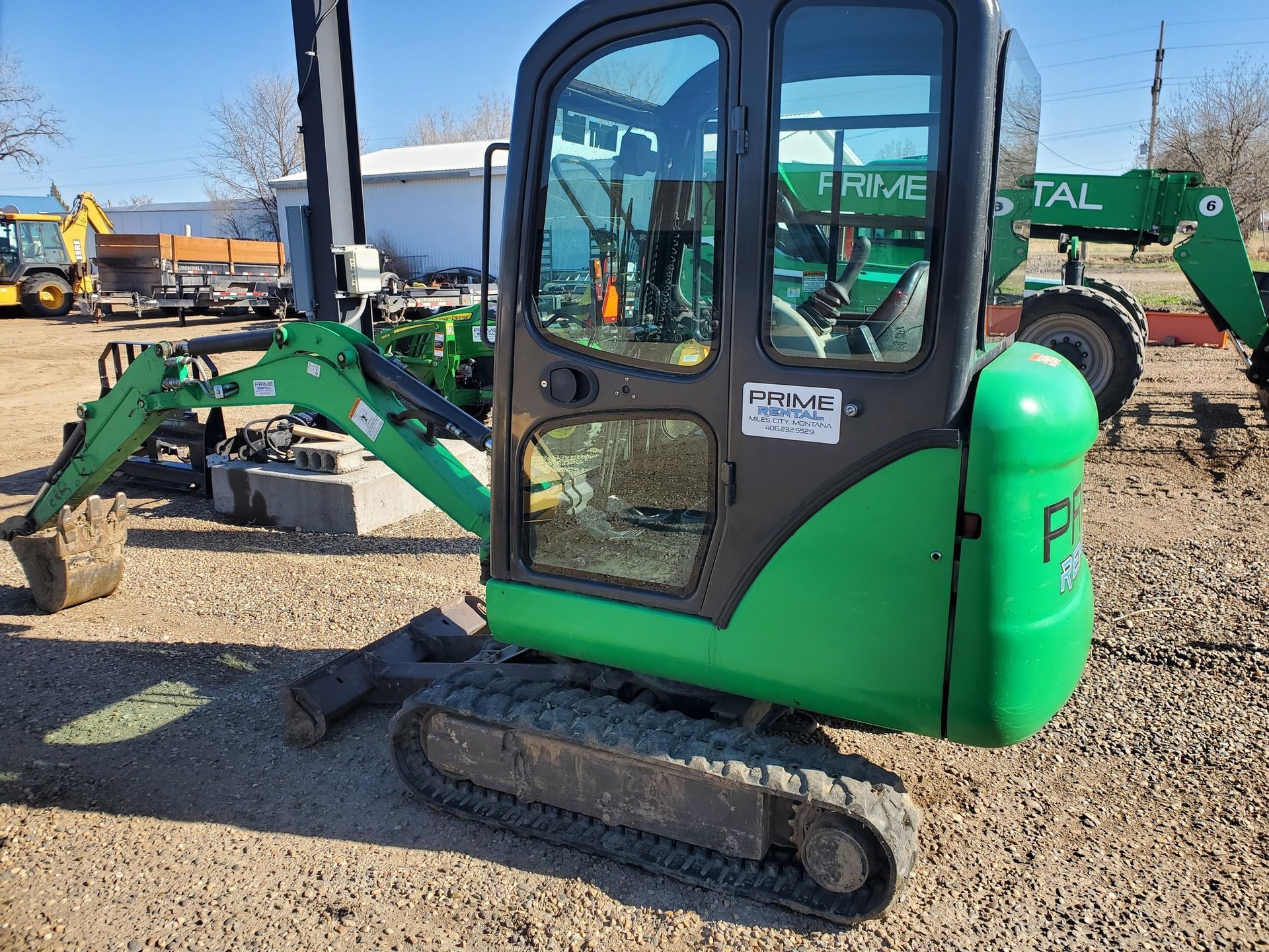 A green and black excavator is parked in a gravel lot.