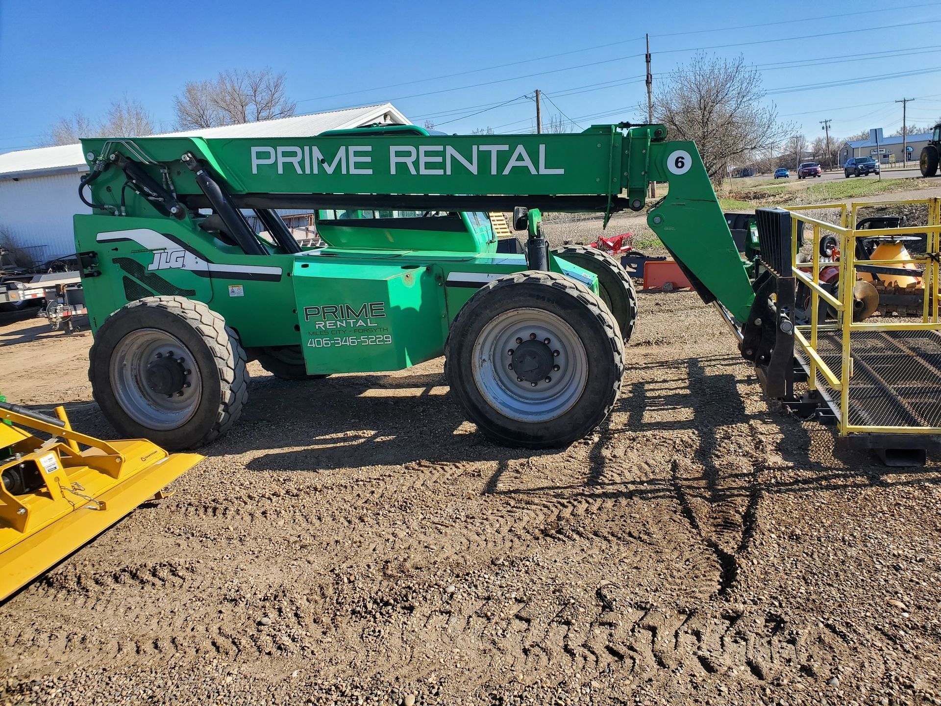 A green forklift from prime rental is parked in a dirt lot.